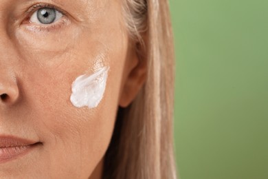 Photo of Senior woman with face cream on green background, closeup