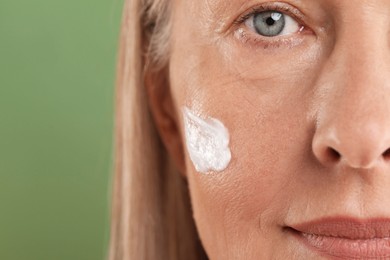 Senior woman with face cream on green background, closeup