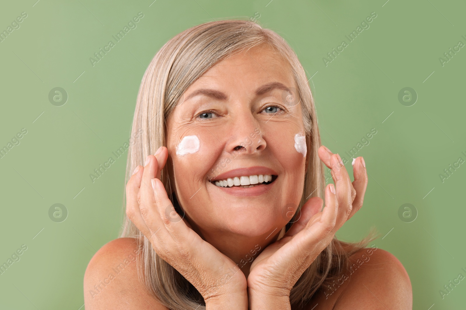 Photo of Senior woman with face cream on green background