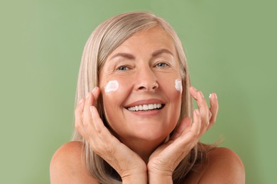 Senior woman with face cream on green background