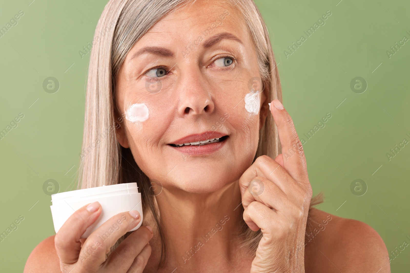 Photo of Senior woman applying face cream on green background, closeup