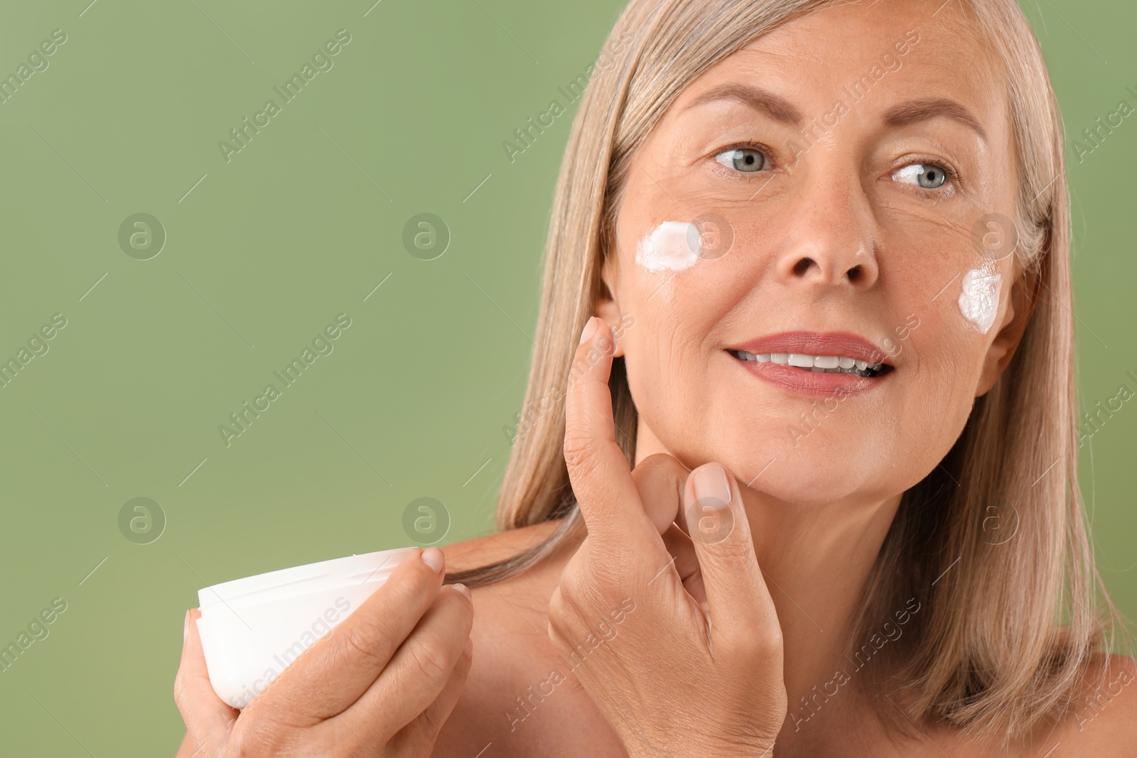 Photo of Senior woman applying face cream on green background, closeup