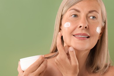 Senior woman applying face cream on green background, closeup