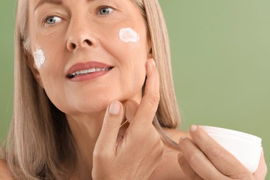 Senior woman applying face cream on green background, closeup