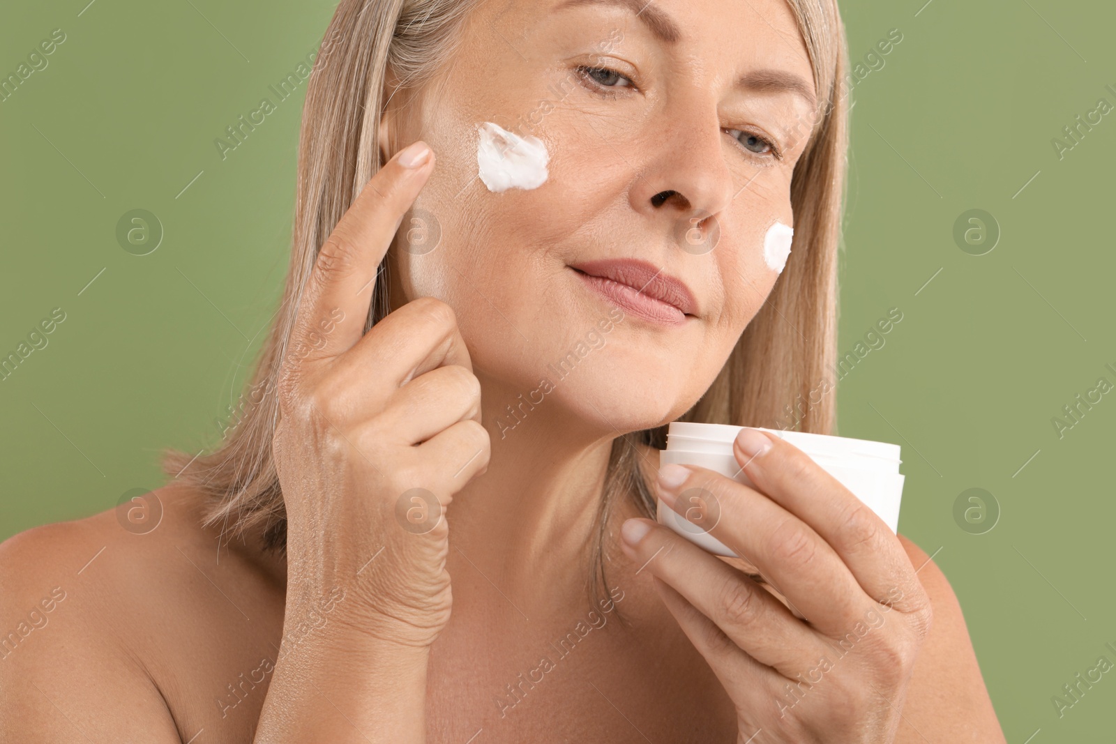 Photo of Senior woman applying face cream on green background, closeup