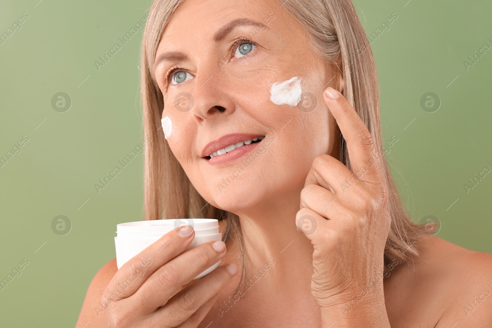 Photo of Senior woman applying face cream on green background, closeup