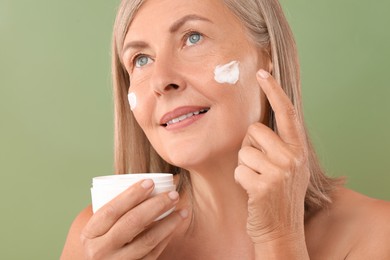 Senior woman applying face cream on green background, closeup