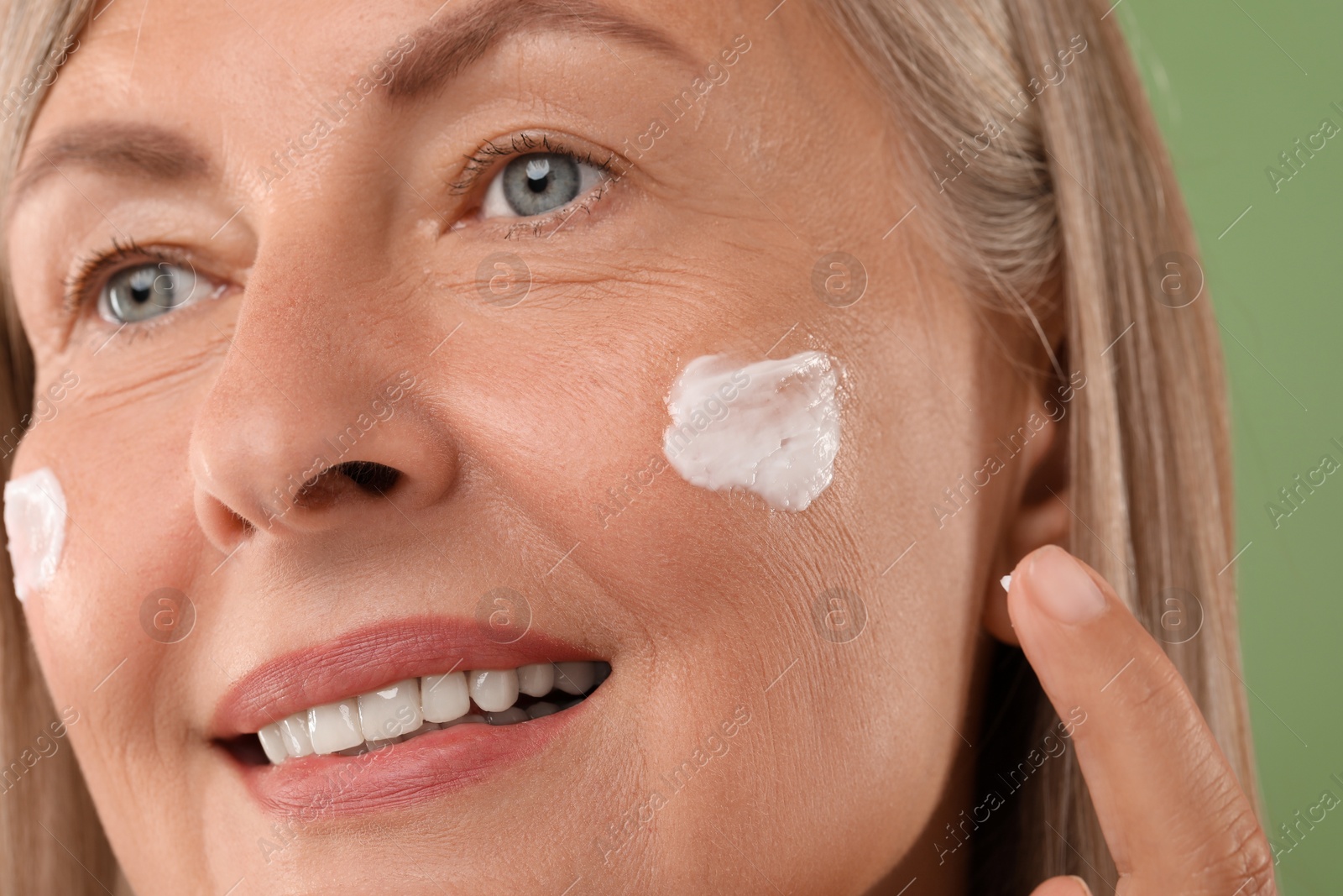 Photo of Senior woman applying face cream on green background, closeup