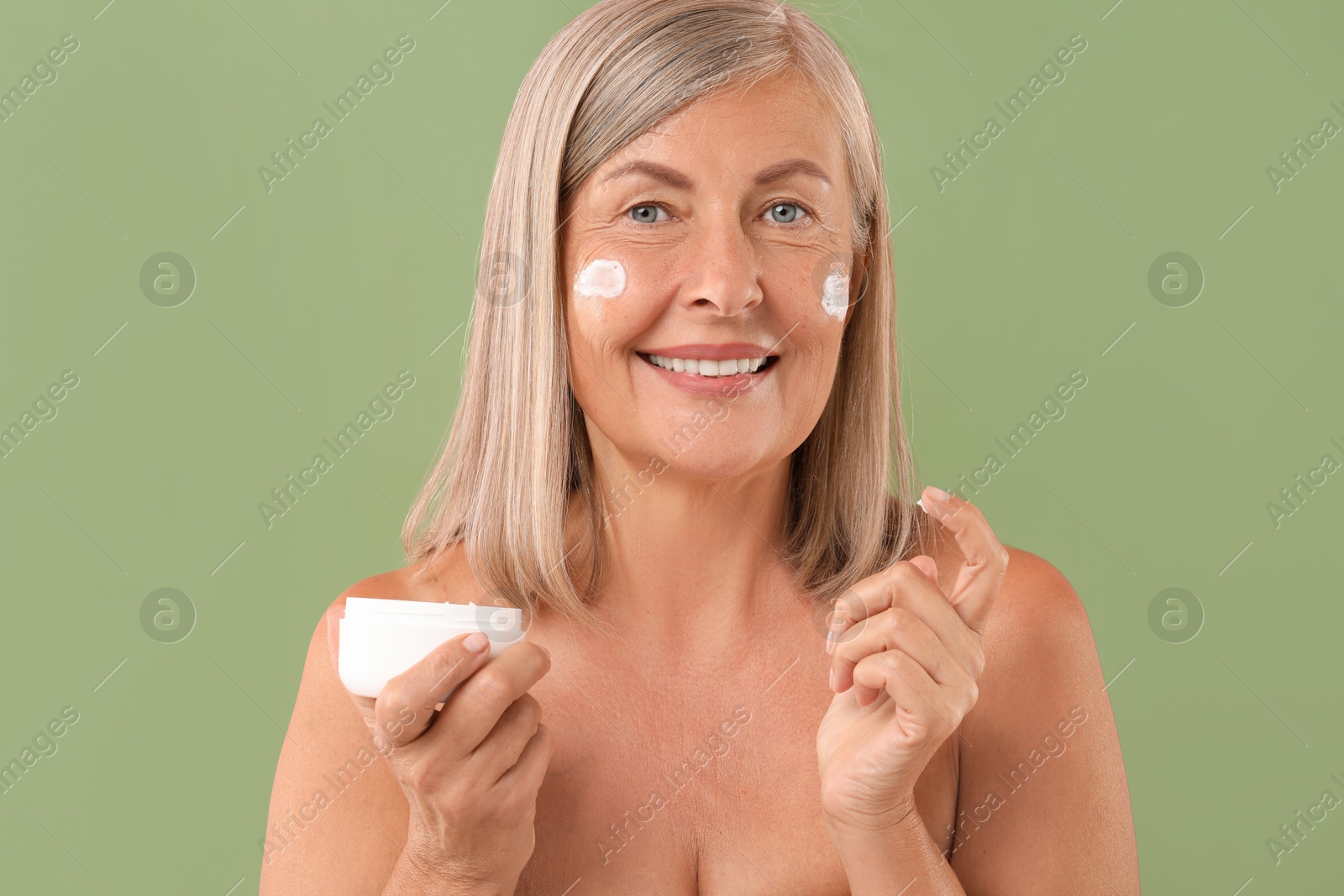 Photo of Senior woman with face cream on green background