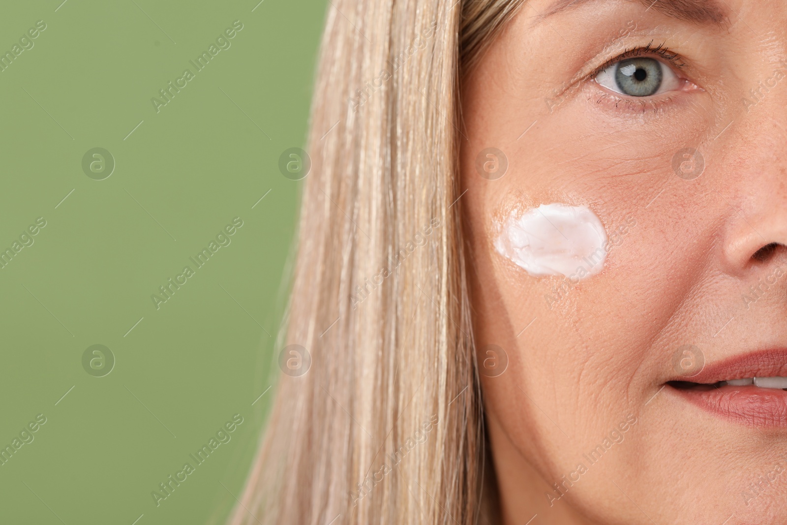 Photo of Senior woman with face cream on green background, closeup