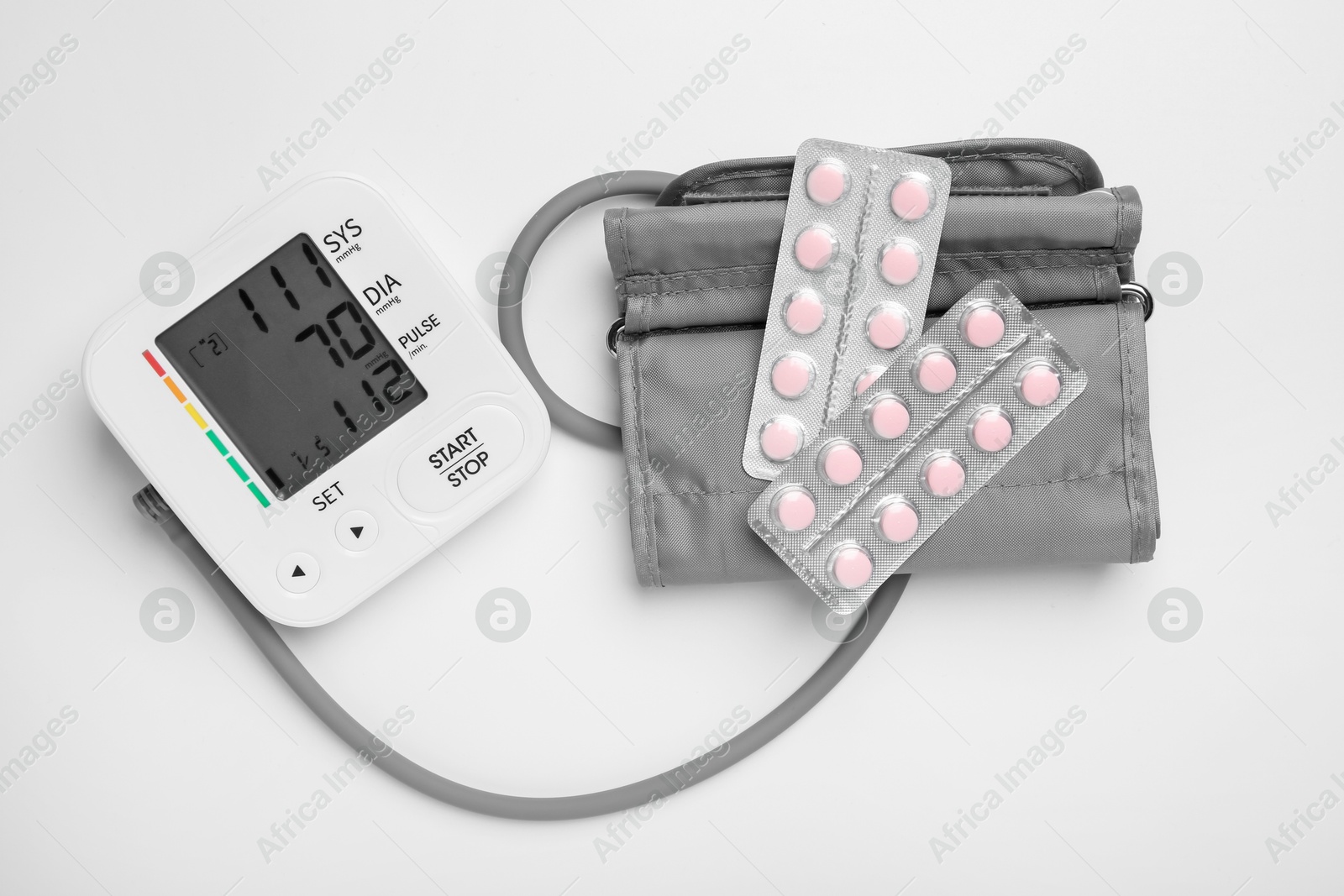 Photo of Blood pressure measuring device and pill blisters on light grey background, flat lay