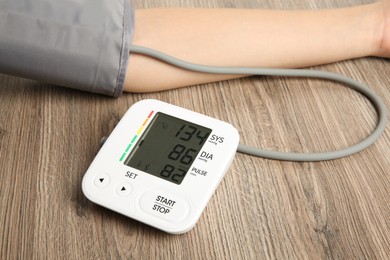 Woman measuring her blood pressure with device at wooden table, closeup