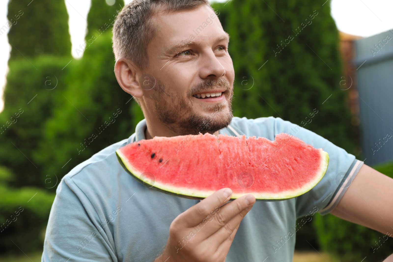 Photo of Happy man with slice of juicy watermelon outdoors