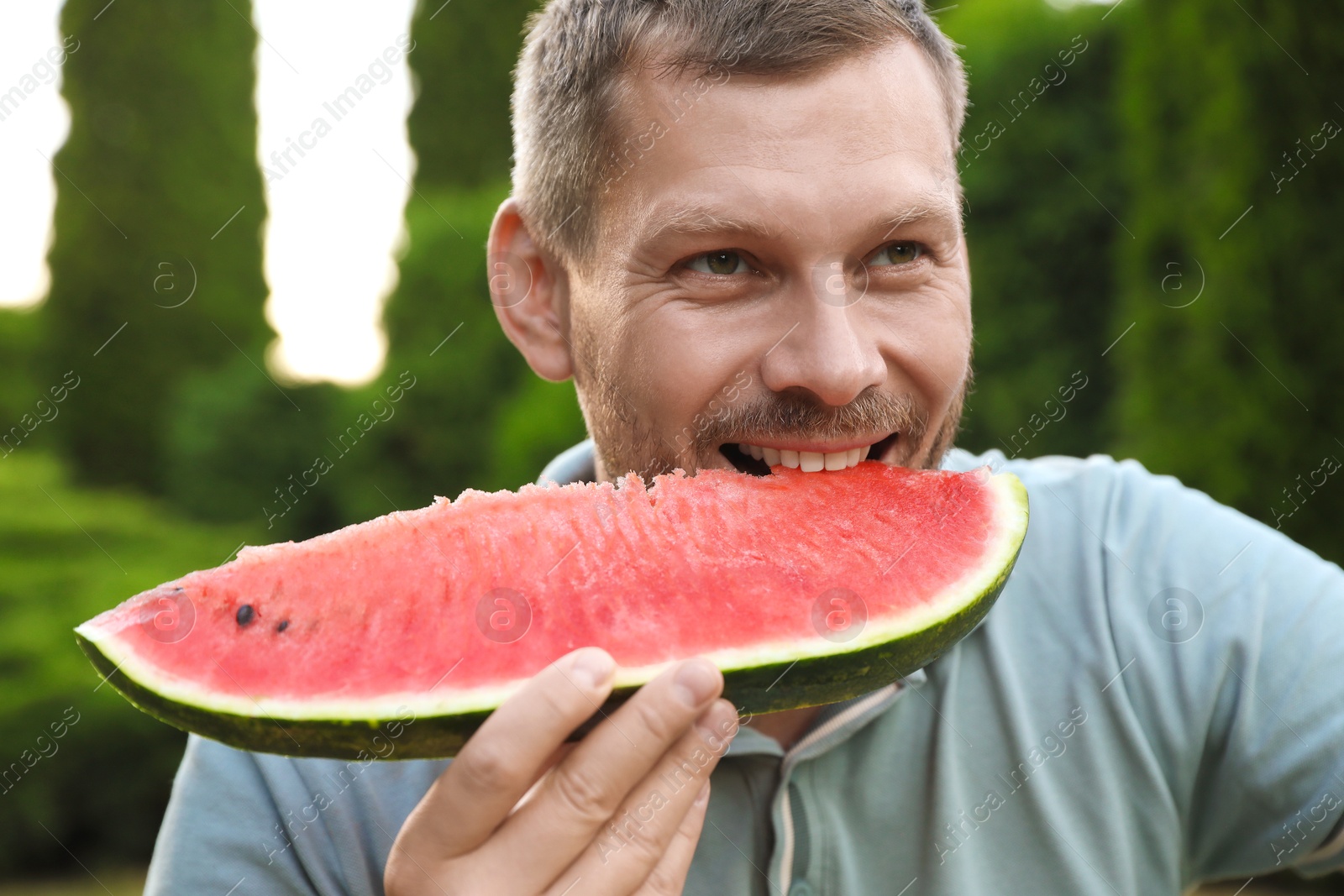 Photo of Happy man eating juicy watermelon outdoors, closeup