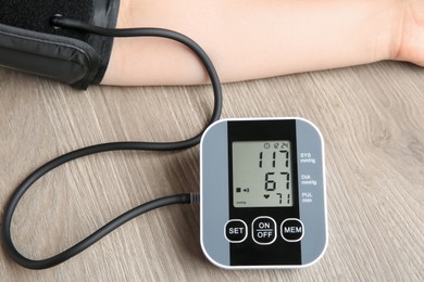 Photo of Woman measuring blood pressure at wooden table, closeup