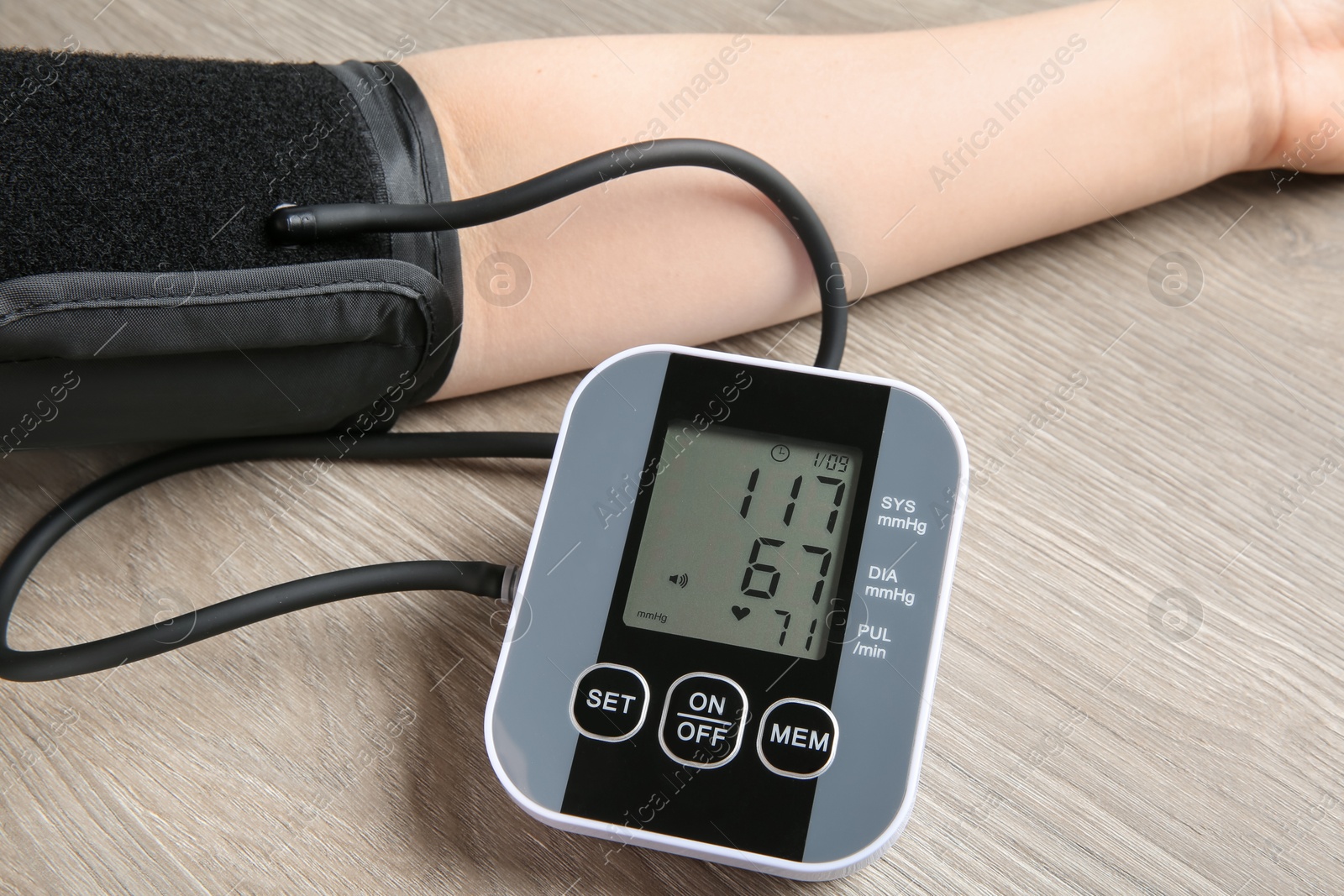 Photo of Woman measuring blood pressure at wooden table, closeup