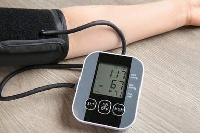 Photo of Woman measuring blood pressure at wooden table, closeup