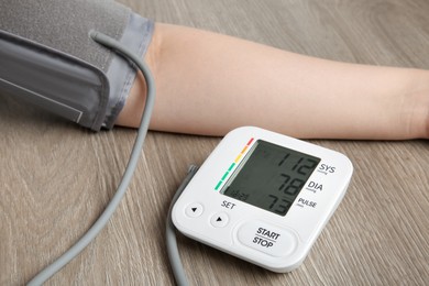 Photo of Woman measuring blood pressure at wooden table, closeup