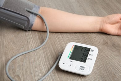 Photo of Woman measuring blood pressure at wooden table, closeup