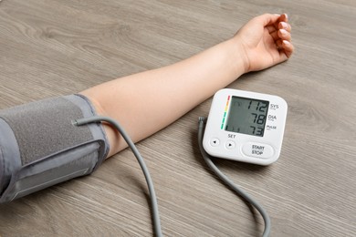 Photo of Woman measuring blood pressure at wooden table, closeup