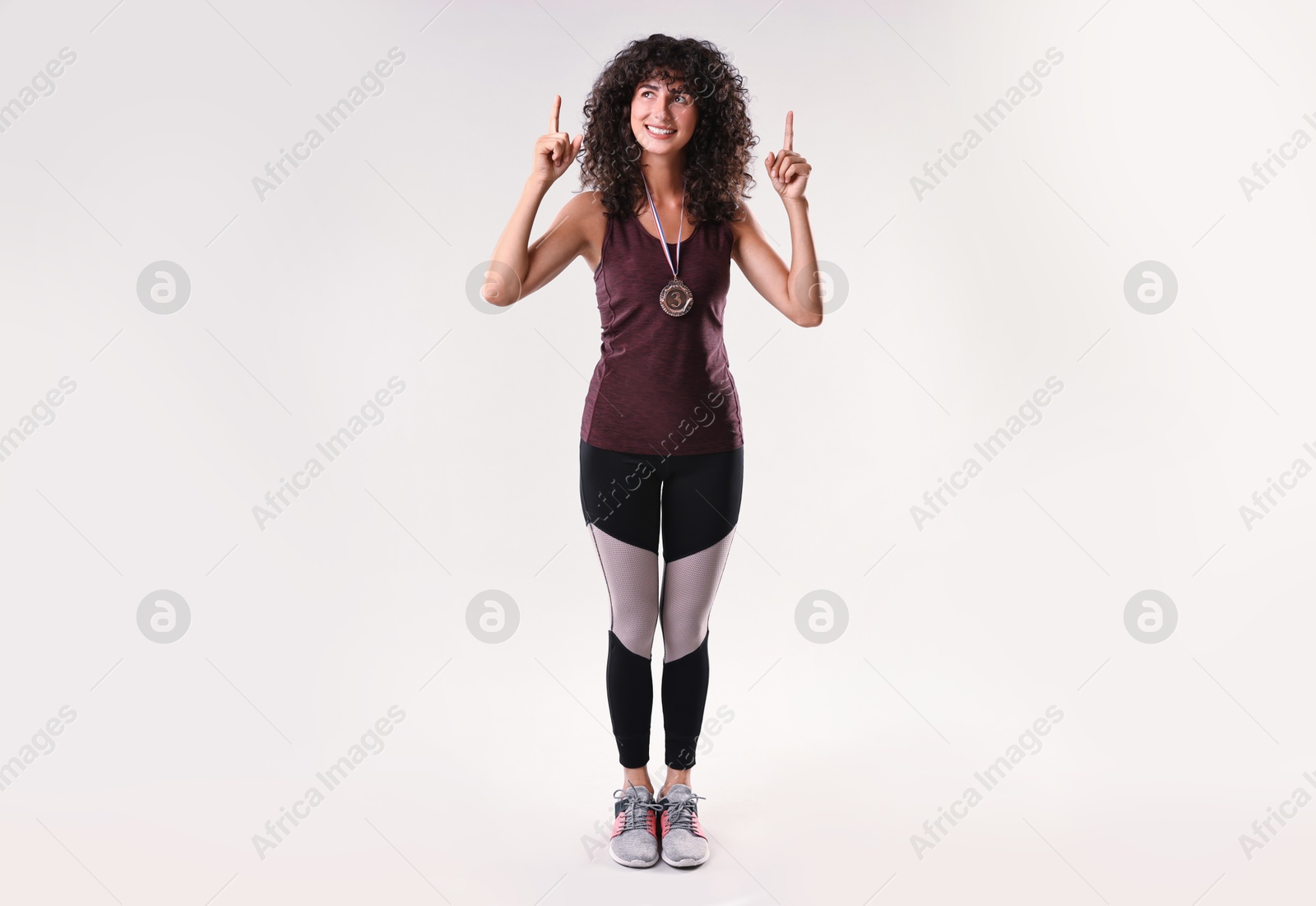 Photo of Happy winner with bronze medal pointing upwards on light grey background