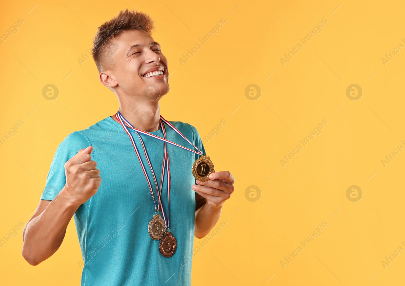 Photo of Happy winner with different medals on yellow background. Space for text