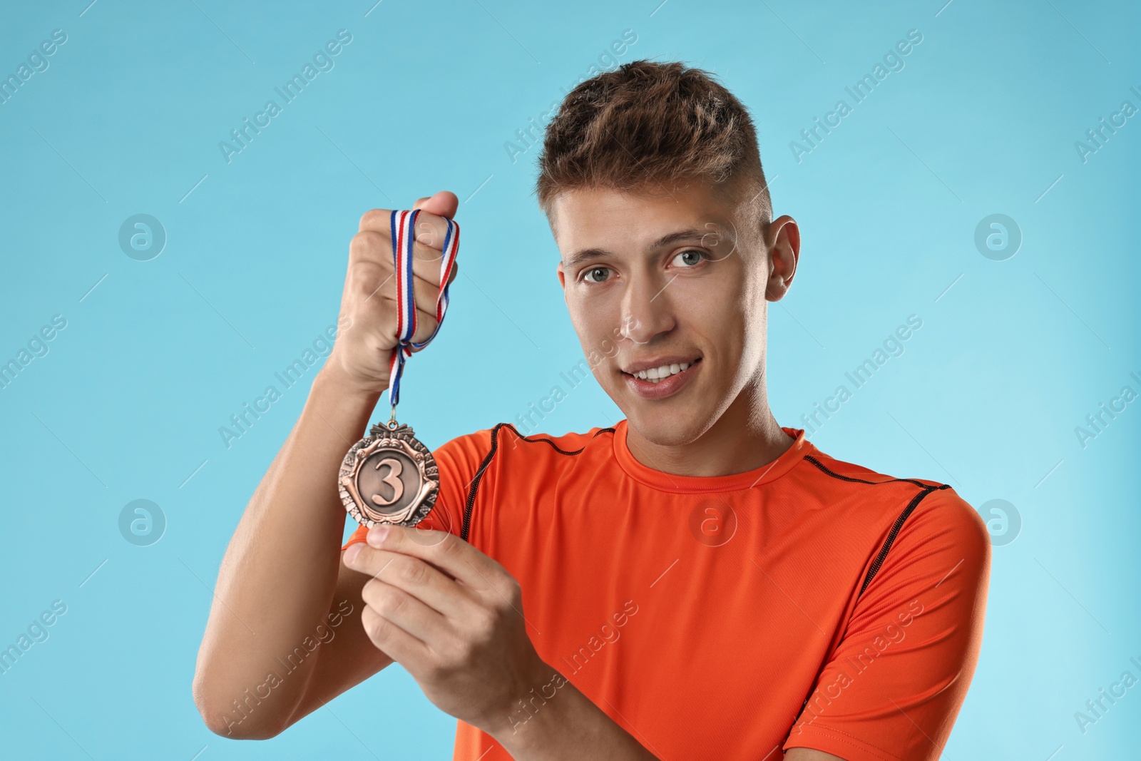 Photo of Handsome winner with bronze medal on light blue background