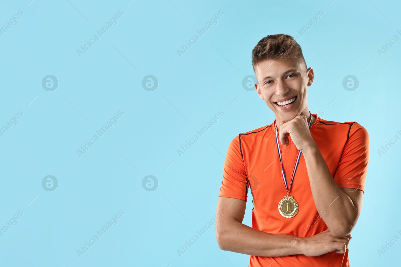 Photo of Happy winner with golden medal on light blue background. Space for text