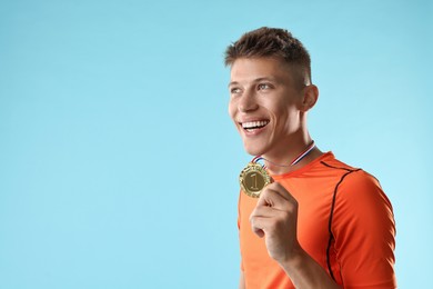 Photo of Happy winner with golden medal on light blue background. Space for text