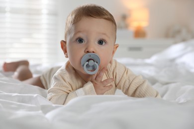 Photo of Cute little baby with pacifier on bed indoors