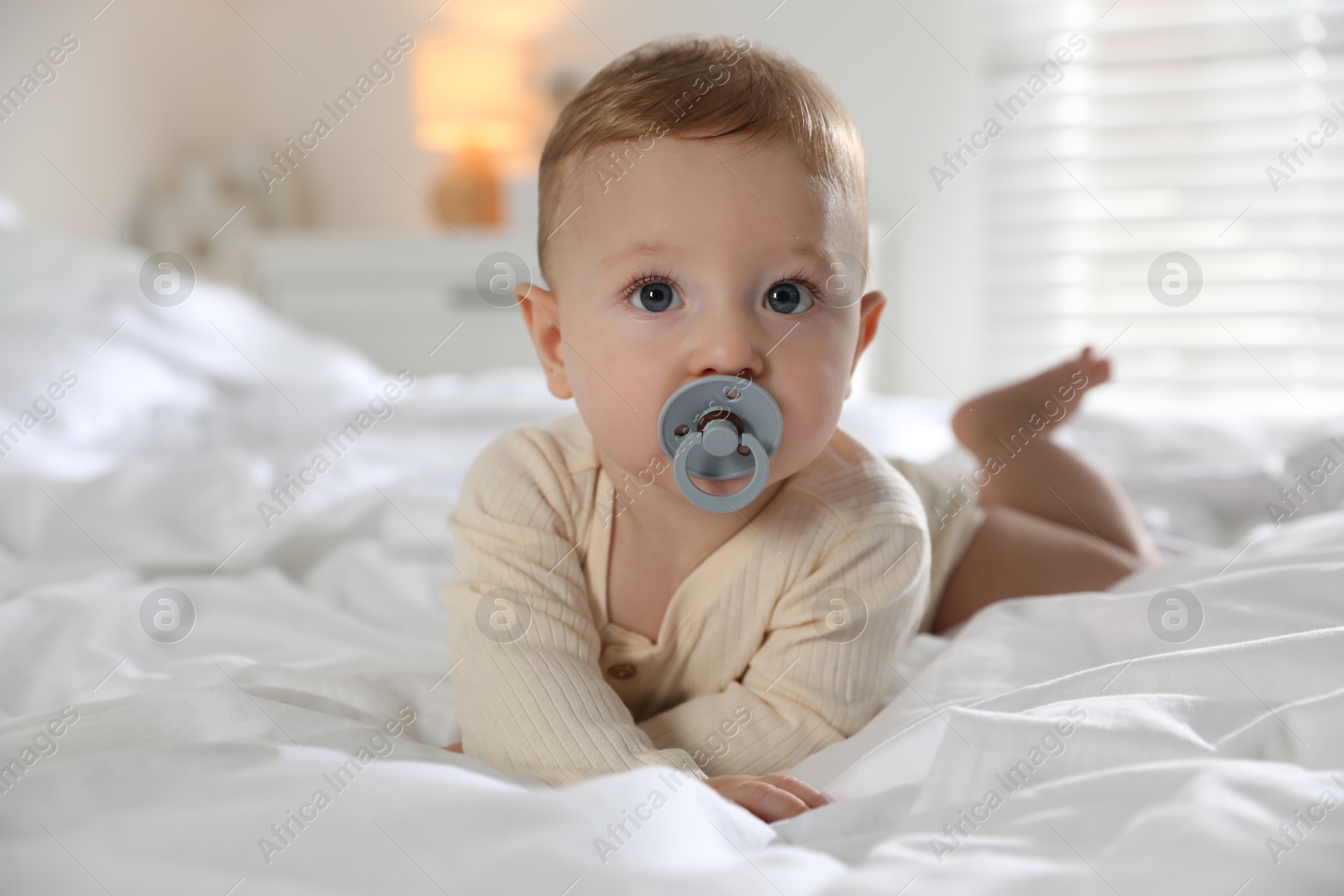 Photo of Cute little baby with pacifier on bed indoors