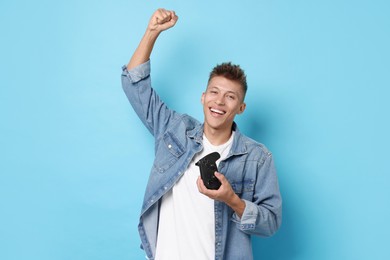 Happy young man with controller on light blue background