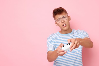 Young man playing video games with controller on pink background, space for text