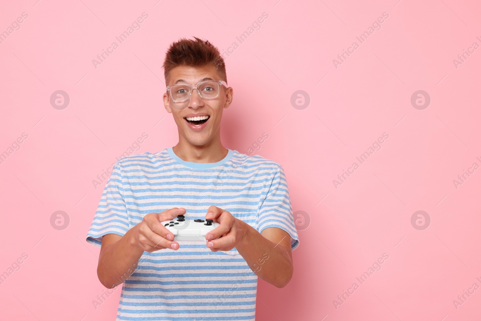 Photo of Happy young man playing video games with controller on pink background, space for text