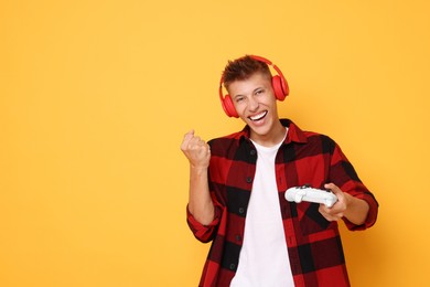 Photo of Happy young man in headphones with controller on orange background, space for text