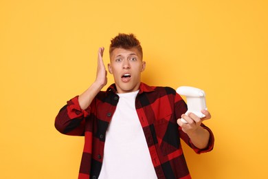 Surprised young man with controller on orange background