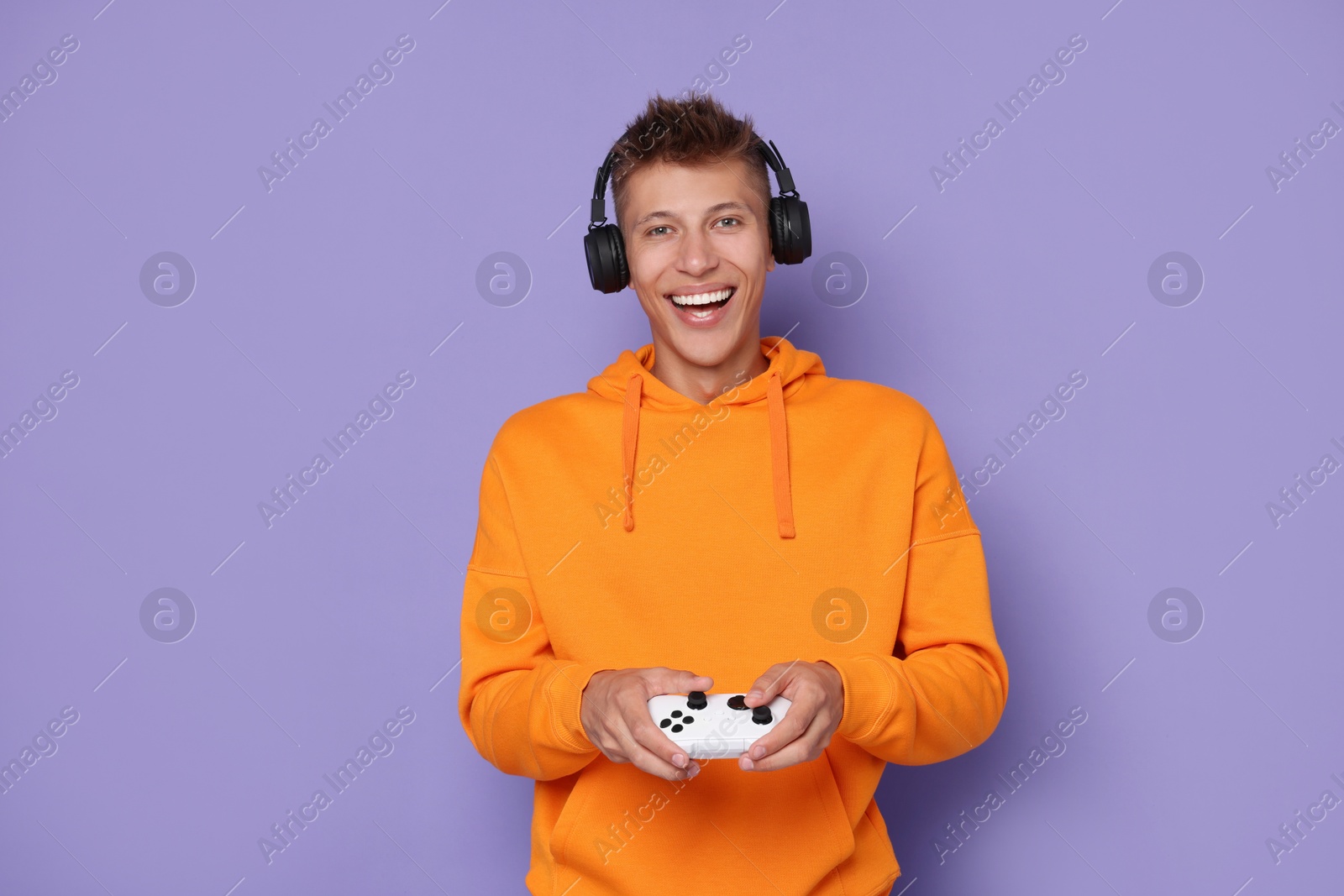 Photo of Happy young man in headphones playing video games with controller on violet background