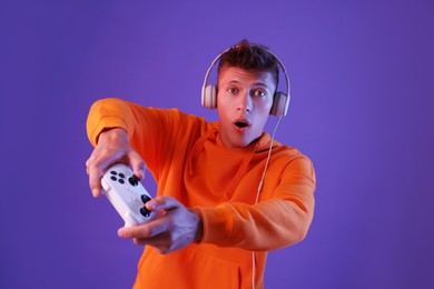 Young man playing video games with controller on violet background