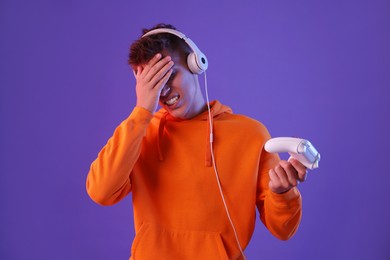 Unhappy young man with controller on violet background