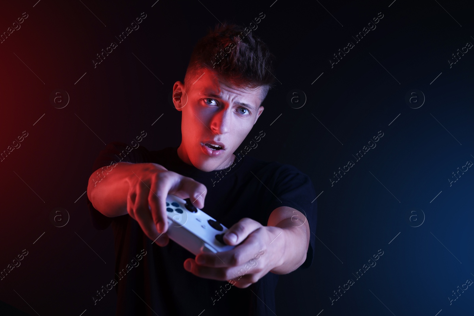 Photo of Young man playing video games with controller on black background