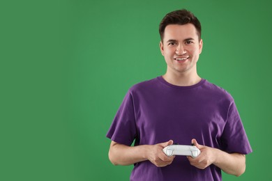 Happy young man playing video games with controller on green background, space for text