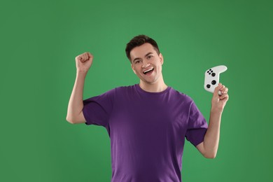 Happy young man playing video games with controller on green background