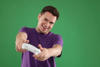 Photo of Happy young man playing video games with controller on green background, space for text