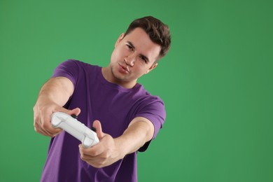 Photo of Young man playing video games with controller on green background, space for text