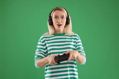 Photo of Surprised woman in headphones playing video games with controller on green background