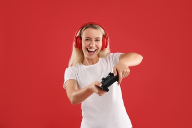 Photo of Happy woman in headphones playing video games with controller on red background