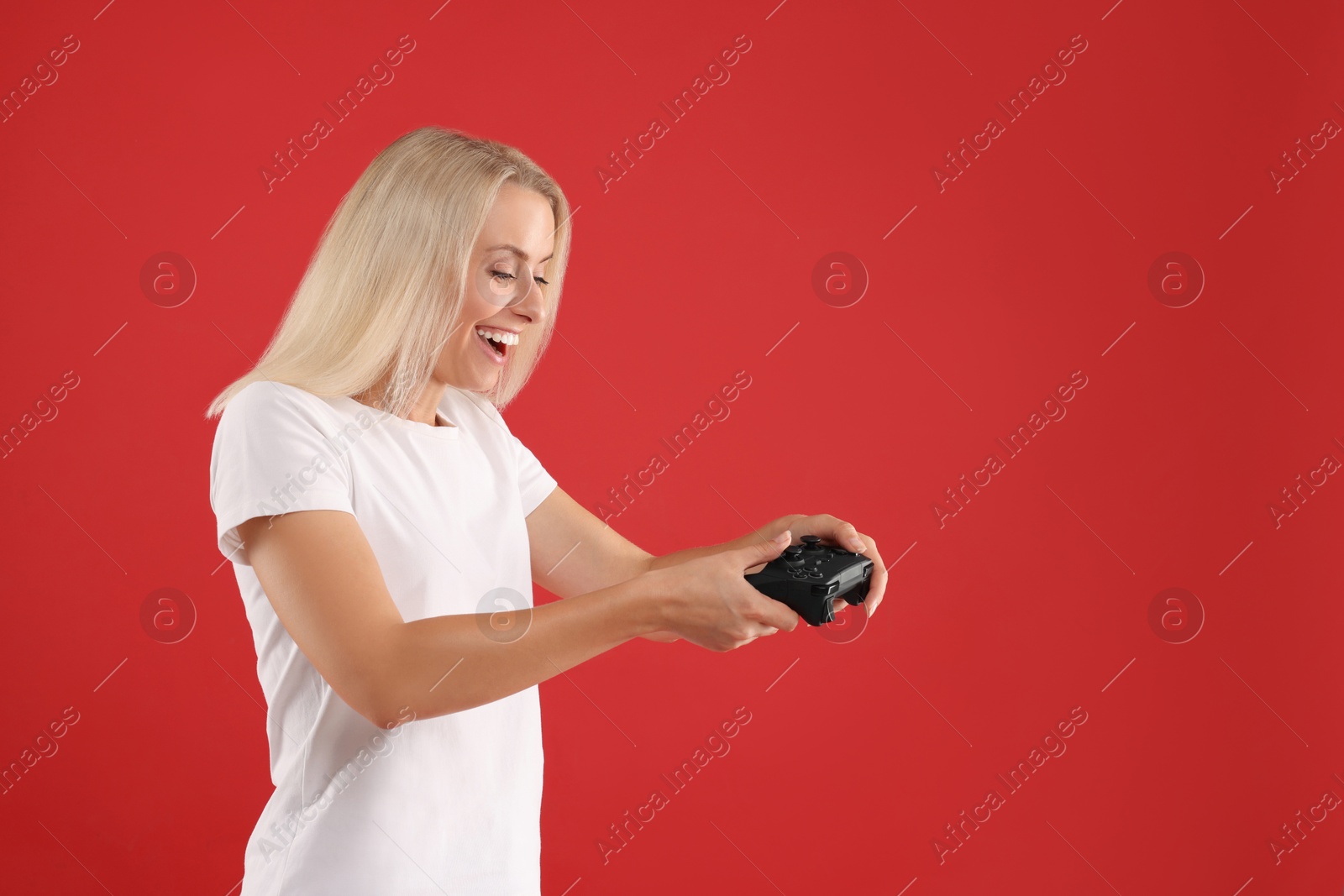 Photo of Happy woman playing video games with controller on red background, space for text