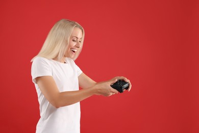 Happy woman playing video games with controller on red background, space for text