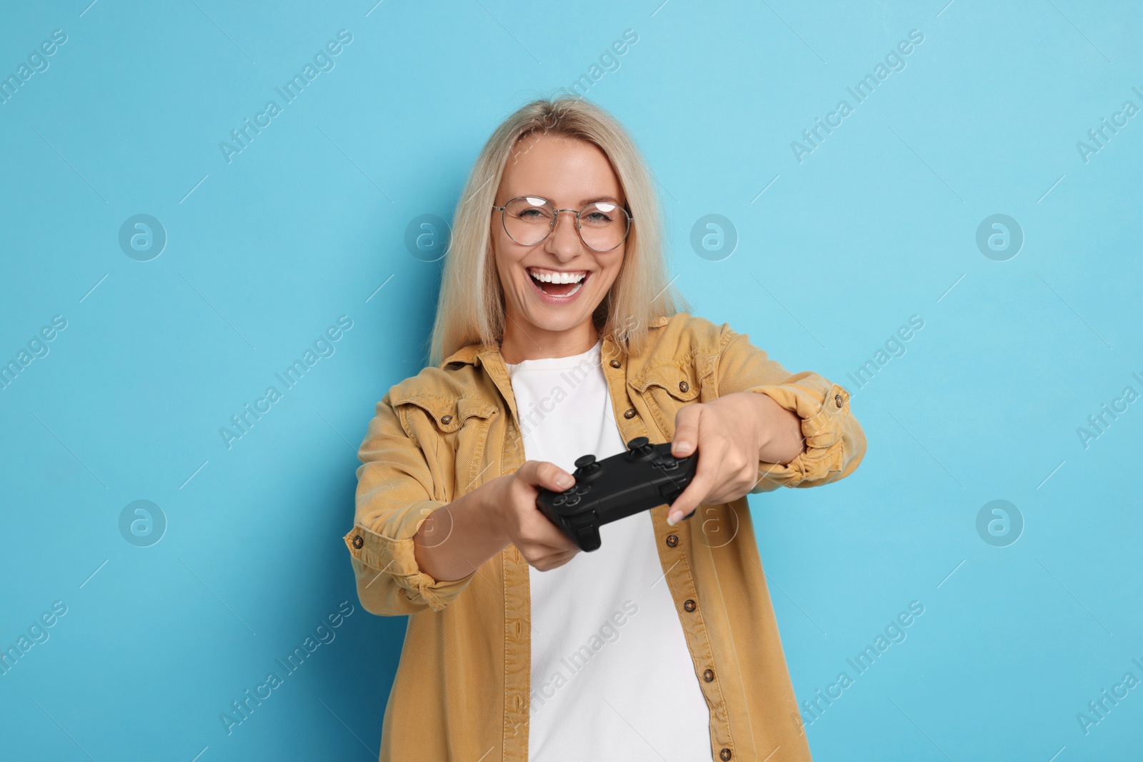 Photo of Happy woman playing video games with controller on light blue background