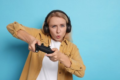 Woman in headphones playing video games with controller on light blue background, space for text